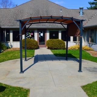 A building entrance with a metal canopy and a concrete pathway surrounded by greenery.
