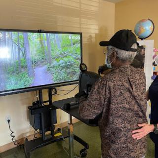An elderly individual engages with a virtual reality nature experience, guided by a caregiver.