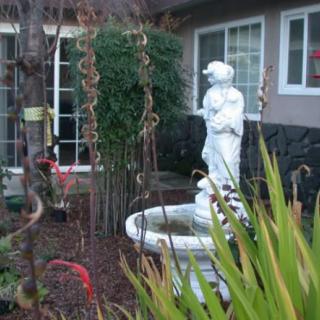 A garden scene featuring a statue fountain surrounded by plants in front of a house.