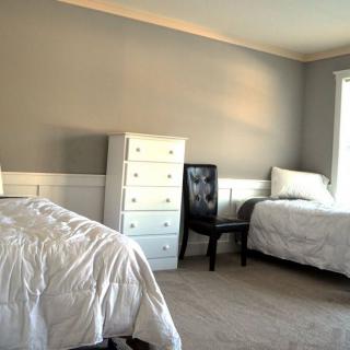 A minimalist bedroom with two beds, a dresser, and a chair in neutral tones.