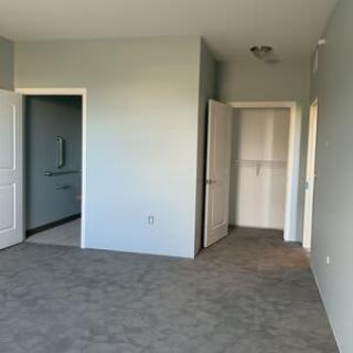 An empty room with carpeted flooring and open doors leading to adjacent areas.