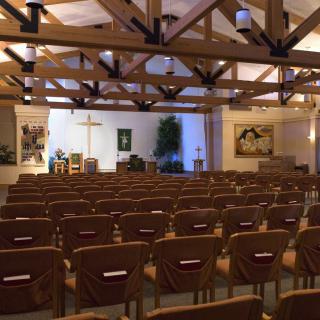 Interior view of a church with rows of chairs facing the altar and a cross.