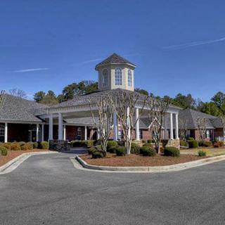 A building with a circular driveway, surrounded by trees and landscaping under a clear blue sky.
