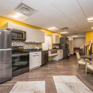 A modern kitchen with stainless steel appliances, yellow walls, and a seating area.