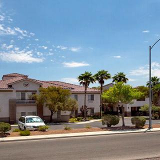 A suburban residential building with palm trees and a parked car on a sunny day.