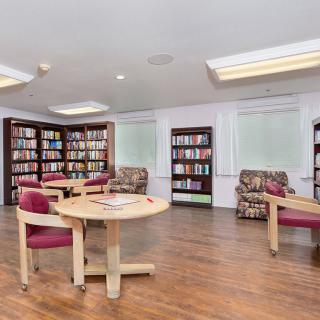 A cozy library reading area with round tables, chairs, and bookshelves lining the walls.