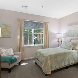 A cozy bedroom with a neatly made bed, an armchair, and soft natural light coming through the window.