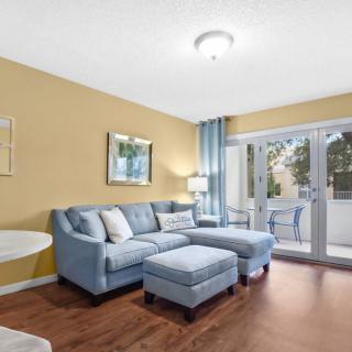 A modern living room with a blue sectional sofa and wooden flooring, featuring large sliding glass doors opening to a balcony.