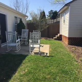 A sunny backyard patio with rocking chairs and a small grassy area.