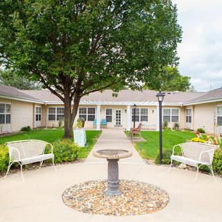 A serene courtyard with a circular pathway, benches, and a central fountain surrounded by greenery.
