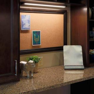 A cozy kitchen corner with a granite countertop, corkboard, and warm lighting.