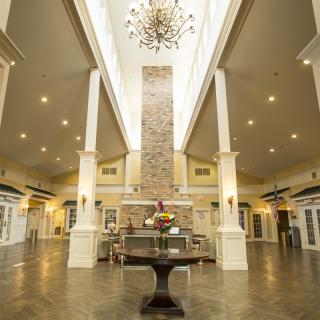 A spacious and elegantly designed lobby featuring a high ceiling with a central chandelier and symmetrical columns.