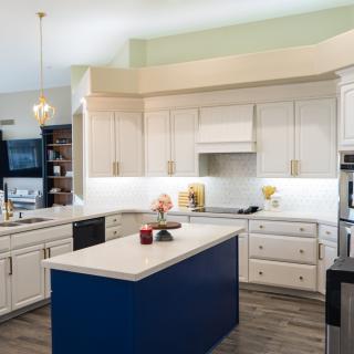 A modern kitchen featuring white cabinetry and a blue-accented island, complemented by pendant lighting and wood flooring.
