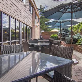 A cozy outdoor patio area with tables and chairs, shaded by large umbrellas, surrounded by greenery.