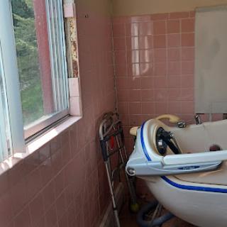 A cozy bathroom featuring a bathtub and pink tiled walls, with sunlight streaming in through the window.