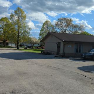 A peaceful residential scene with a house, trees, and a parking area under a partly cloudy sky.