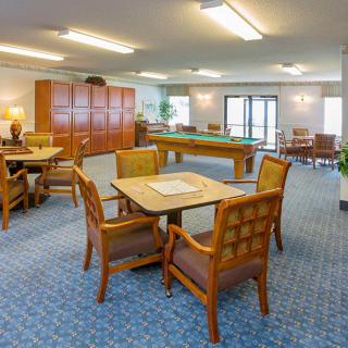 A spacious community room featuring a seating area with tables and chairs, and a billiards table.