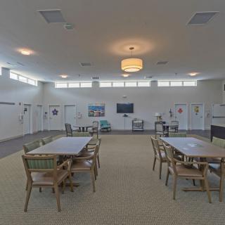 A spacious and well-lit interior room featuring tables and chairs, with a television on the wall.