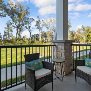 A cozy patio with outdoor chairs and a small table overlooking a grassy area and trees.