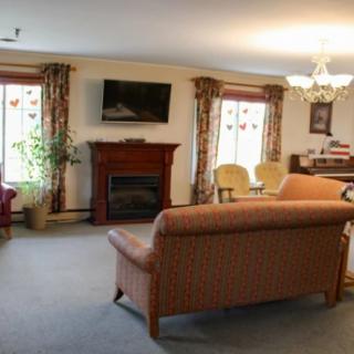 A cozy living room with a sofa, fireplace, and television, decorated with curtains and illuminated by a chandelier.
