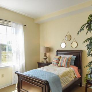 A cozy bedroom with a single bed, bright cushions, and decorative mirrors on the wall.