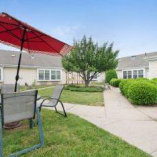 A peaceful outdoor patio area with chairs, a red umbrella, and landscaped garden.