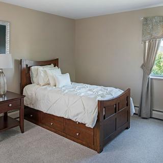 A cozy bedroom featuring a wooden bed with white bedding, a nightstand with a lamp, and a window with curtains.