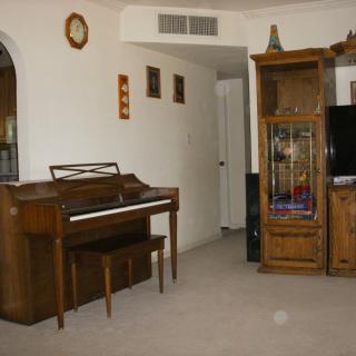 A cozy living room featuring a piano, wooden furniture, and a television.