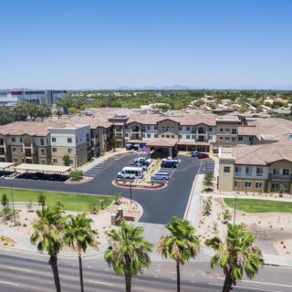 Aerial view of a large building complex with a parking lot and palm trees in a suburban area.