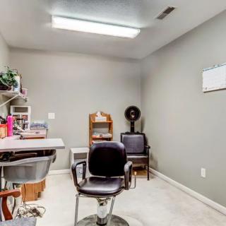 A small hair salon setup with a chair, desk, and shelves.