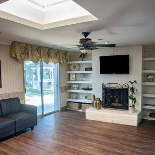 A cozy living room with a fireplace, TV, and built-in shelves, featuring a ceiling fan and a large skylight.