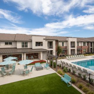 A modern apartment complex featuring a pool and outdoor seating area, surrounded by well-maintained landscaping.
