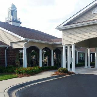 A building with a covered entrance and columns, surrounded by well-maintained landscaping.