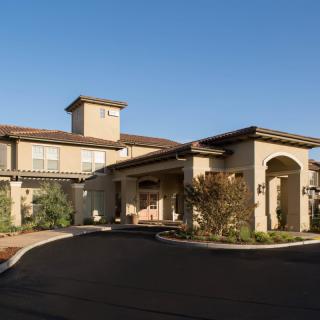 A residential building with a well-maintained driveway and landscaping under a clear blue sky.