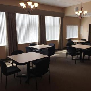 A quiet room with several tables and chairs, featuring large windows and chandeliers.