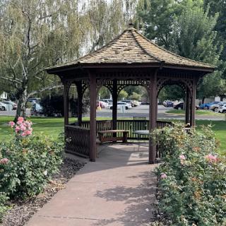 A charming wooden gazebo surrounded by blooming flowers in a peaceful park setting.