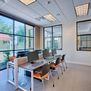A modern office workspace with desks and computers, featuring large windows and ample natural light.
