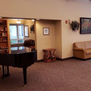 A cozy lobby area featuring a grand piano, bookshelf, and comfortable seating.