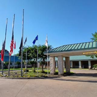 An entrance view featuring a variety of flags in front of a building under a clear blue sky.