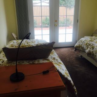 A cozy bedroom with twin beds and a desk lamp, featuring glass doors that allow natural light to fill the room.