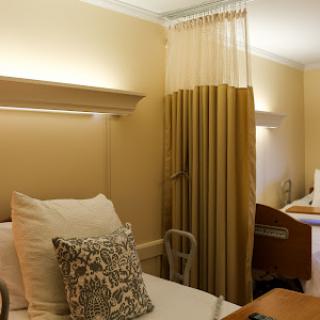 A serene hospital room featuring two beds adorned with decorative pillows and soft lighting.