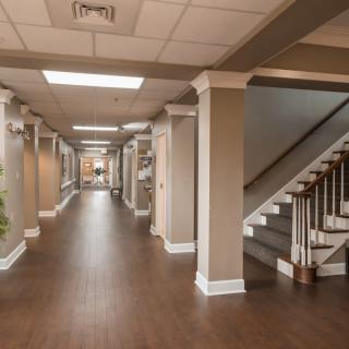 A spacious and well-lit hallway with wooden flooring, featuring stairs on the right.