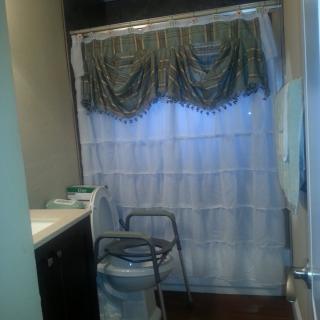 A bathroom with a white shower curtain and an accessible chair.