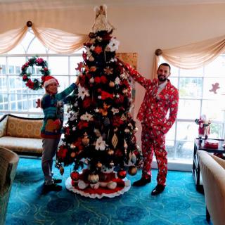 Two people standing next to a beautifully decorated Christmas tree in a festive living room.