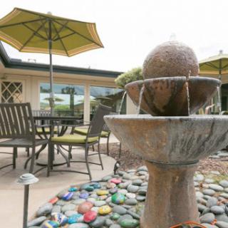 A serene outdoor space featuring a decorative fountain, comfortable seating, and vibrant umbrellas.