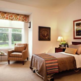 A cozy bedroom with a single bed, armchair, and large window.