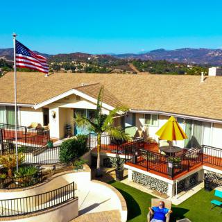 A scenic view of a house with a spacious patio and an American flag flying, set against a backdrop of rolling hills on a sunny day.