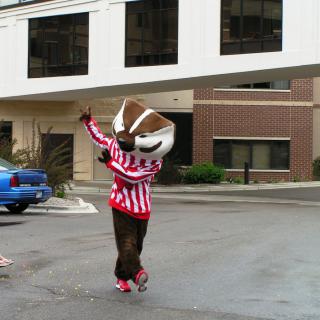 A person in a mascot costume wearing a striped shirt is standing outdoors on the street.