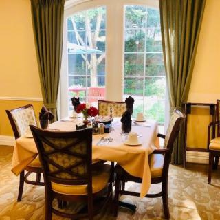 An elegant dining area with a table set for four, featuring large windows and green curtains.