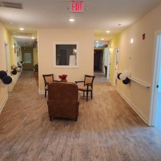 A well-lit hallway with a seating area featuring chairs and a table on a wooden floor.